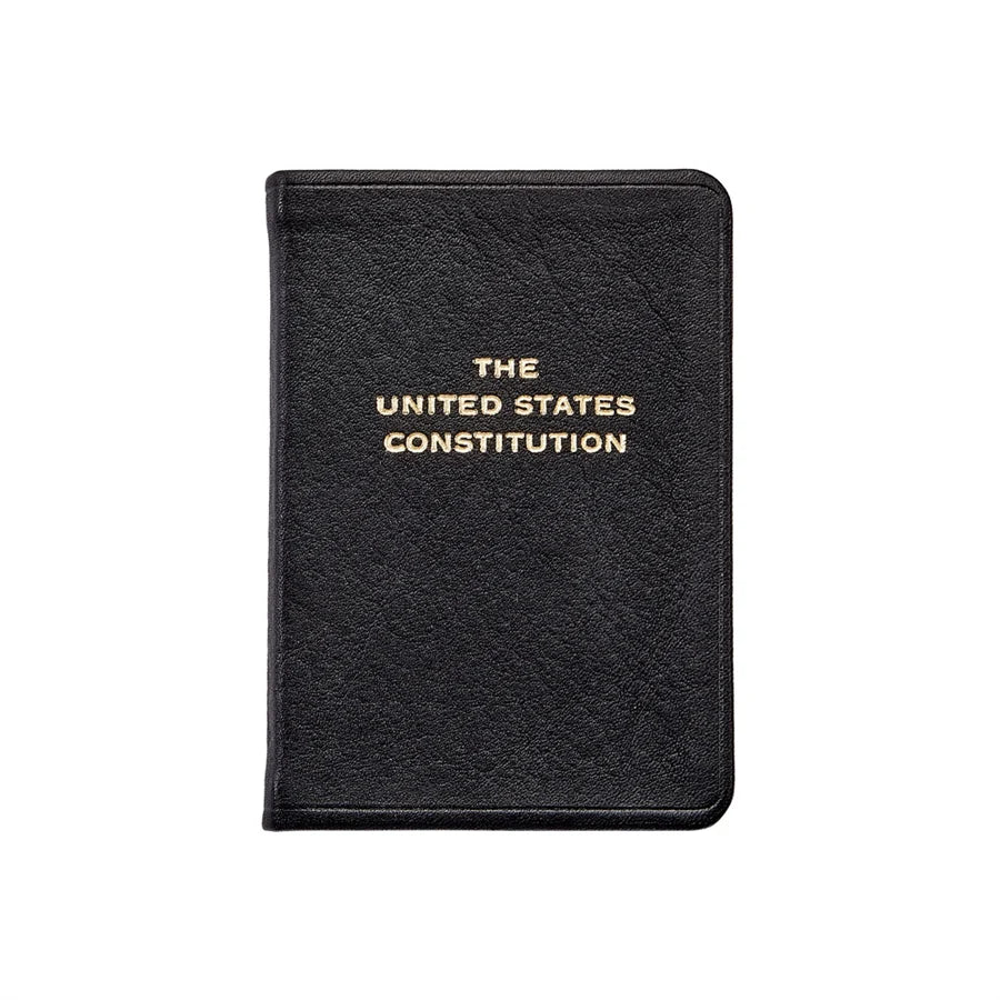 A black, leather‑bound book titled The United States Constitution, with the title stamped in gold lettering, shown against a clean white background.