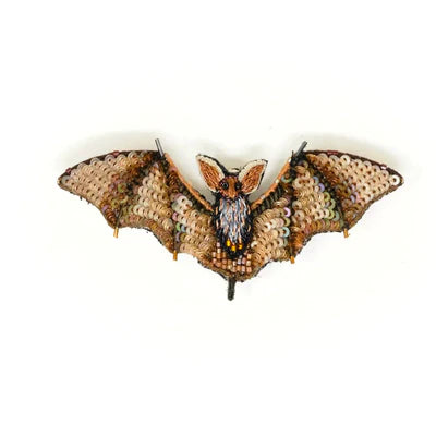 A small bat-shaped brooch with a raised body and wide, outstretched wings. It features detailed hand embroidery in light brown tones, highlighting the wings and oversized ears.
Made with soft fabric and subtle beading, it has a gently textured feel and a metal pin on the back. Each handmade piece varies slightly, making it unique.
