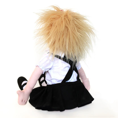 The image shows the doll seated with her back facing the viewer, her short blond hair tousled and playful. She wears Eloise’s iconic outfit—a ruffled white blouse, black pleated skirt, and satin black shoes.