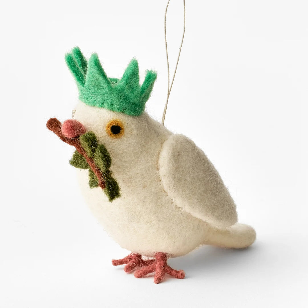 Felt New York City Dove Ornament - A handcrafted needle-felted wool dove stands upright wearing a bright green Statue of Liberty-style crown. It holds a green olive branch with a brown stem in its beak. The dove’s beak and feet are burnt orange, and its eyes have black pupils with yellow irises. A gold hanging loop is attached at the top, allowing the ornament to be displayed. The handmade sculpture combines symbols of peace and liberty.