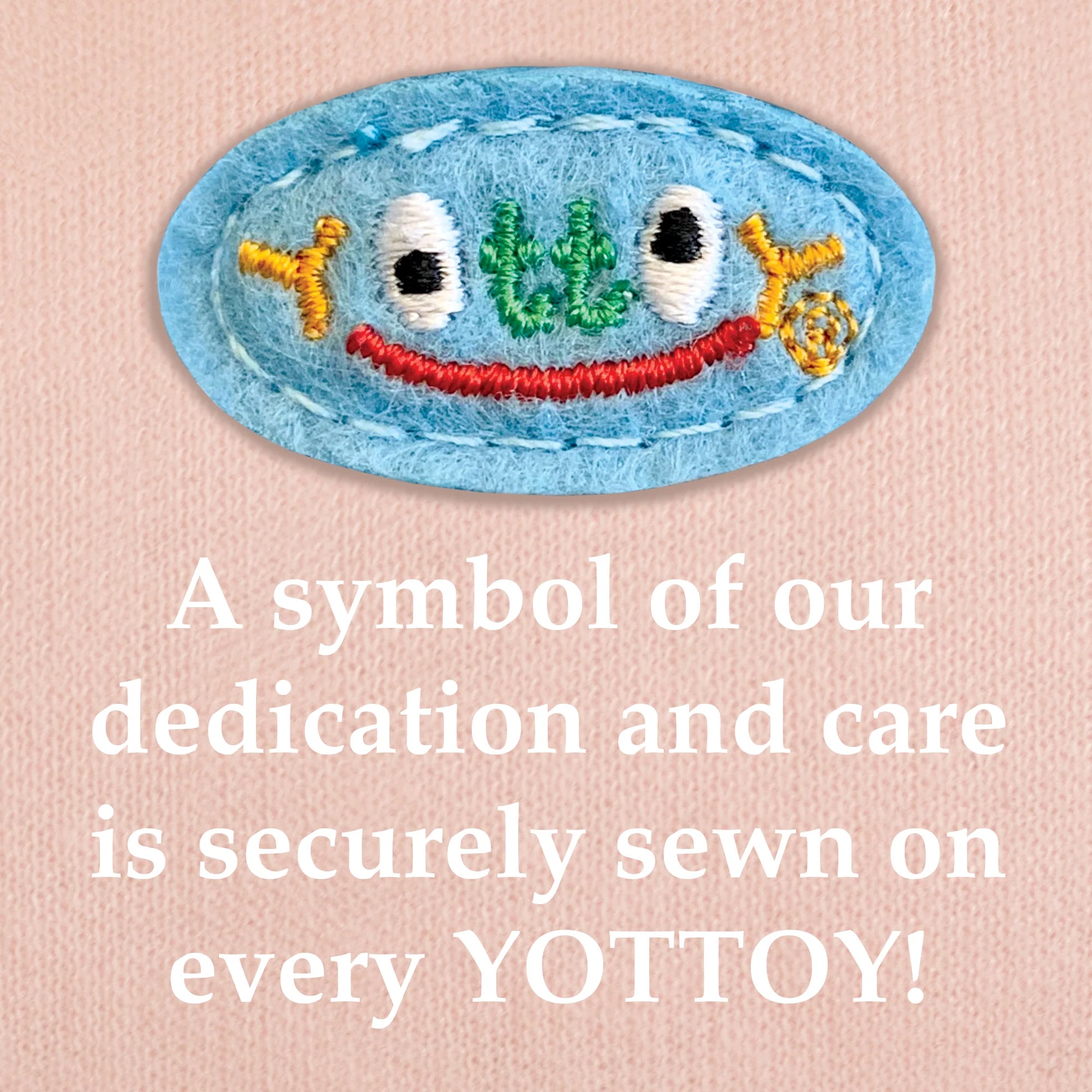The image shows an embroidered blue YOTTOY logo in multicolored stitching with a small red smile, sewn onto pink knit fabric. Below the emblem, bold white text reads: “A symbol of our dedication and care is securely sewn on every YOTTOY!”