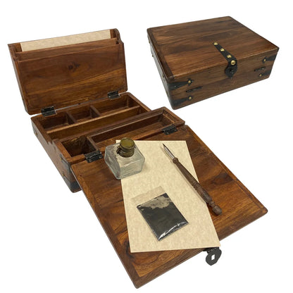 The image shows two views of a weathered, portable teak wood writing desk. In the open view, the lid reveals slotted sections for documents or paper, along with interior storage compartments. The writing flap is open, displaying a wooden pen, a small ink bottle with a distressed brass cap, powdered ink, and parchment‑like paper, reinforcing the desk’s antique, well‑traveled character. Beside it, the second view shows the desk closed, highlighting its compact, portable form.