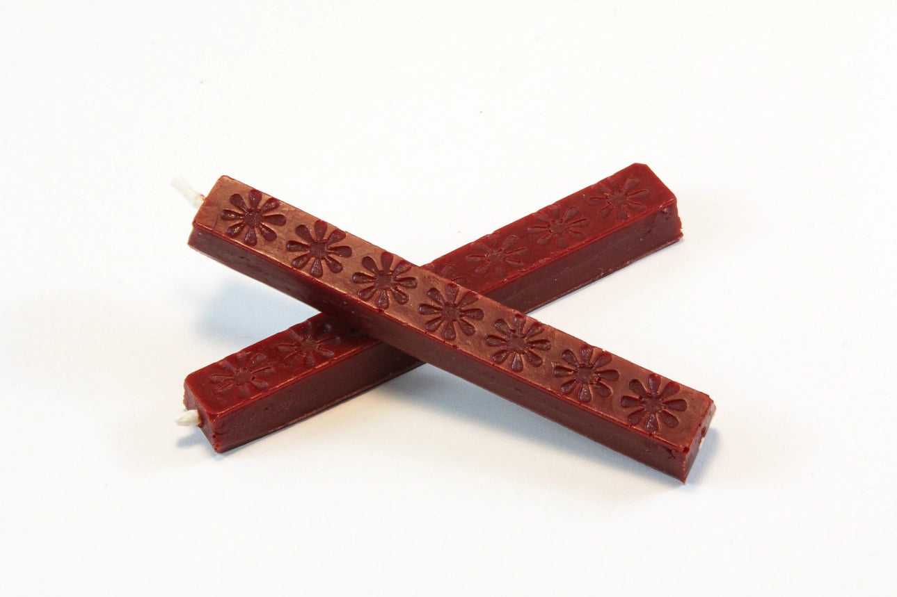 The image shows two 4‑inch burgundy wax sticks on a white background. The wax appears hard and smooth, with subtle daisy‑like embossed patterns. When melted, it becomes thick and pliable, then cools to a slightly flexible, buttery finish designed to resist cracking in the mail.