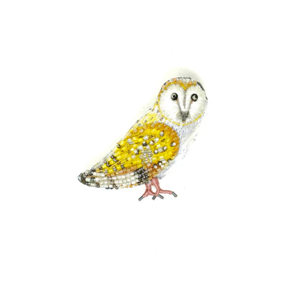 Golden Owl Brooch - A hand embroidered owl brooch with a tall, slightly oval shape. The surface is richly textured, combining soft felt with raised stitching, sequins, and small beads that create a layered, lightly shimmering finish. The owl features a golden color palette with detailed wings, a defined face, and round eyes that stand out through beadwork. A smooth metal pin is attached on the back for fastening. Each piece is handmade, so small variations in texture and detail make every brooch unique.