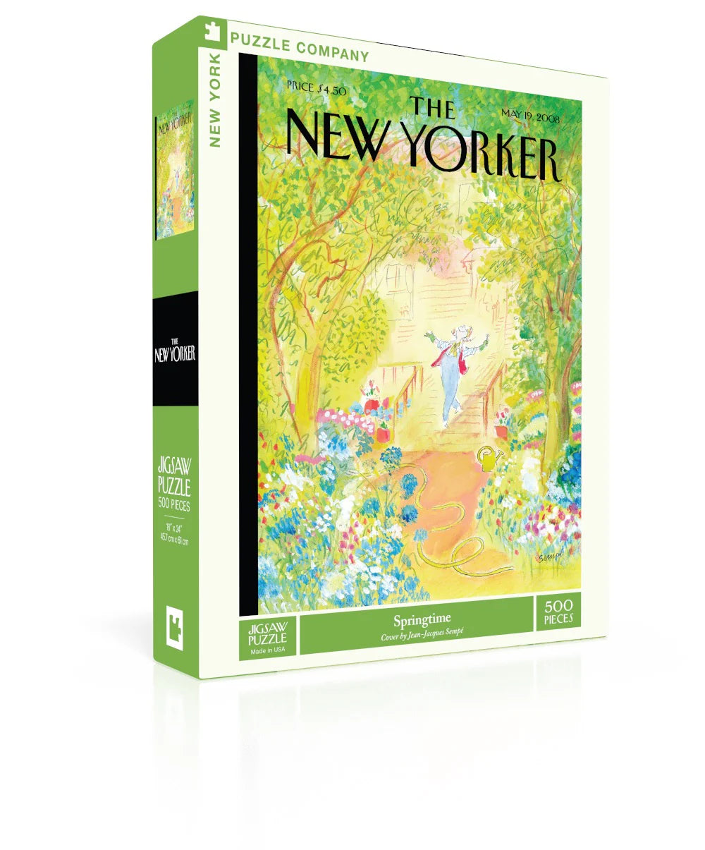 Springtime New Yorker Puzzle — 
The box is a medium‑sized rectangle with smooth, flat surfaces and no raised texture. The front shows a detailed illustration printed completely flat. It depicts a lively city sidewalk filled with blooming flowers, leafy trees, and a woman pausing to admire her garden work. Small figures and buildings line the background, creating a busy springtime street scene. The colors are bright green, blue, pink and orange. 