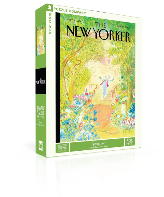 Springtime New Yorker Puzzle — 
The box is a medium‑sized rectangle with smooth, flat surfaces and no raised texture. The front shows a detailed illustration printed completely flat. It depicts a lively city sidewalk filled with blooming flowers, leafy trees, and a woman pausing to admire her garden work. Small figures and buildings line the background, creating a busy springtime street scene. The colors are bright green, blue, pink and orange. 
