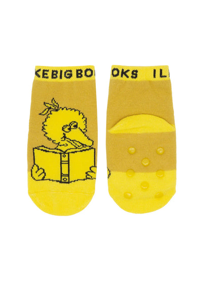A photograph of toddler socks featuring Big Bird. The socks display a simple line‑drawing of Big Bird set against bright yellow background. The other sock is shown from the bottom, displaying rubberized anti‑slip dots across the sole.