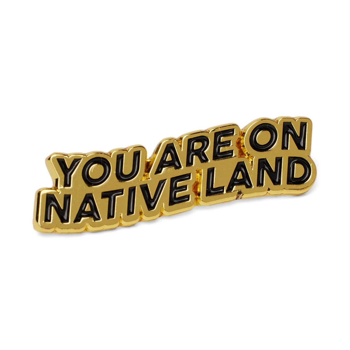 A gold-colored enamel pin with black lettering that reads 'YOU ARE ON NATIVE LAND', shown on a plain white background.