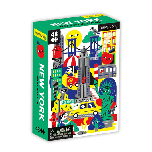 Product title: New York City Mini Puzzle -
A small, brightly colored puzzle box shows playful illustrations of New York City icons, including a water tower, the Empire State Building, the Statue of Liberty, a yellow taxi, and other classic city sights.