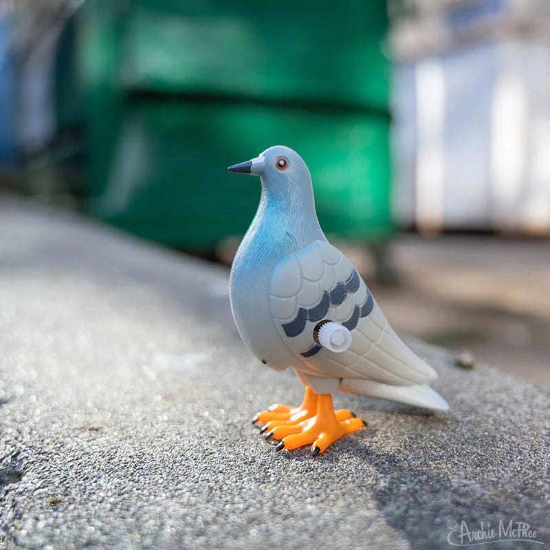 The toy pigeon stands on a real New York curbside, with a green dumpster in the background.