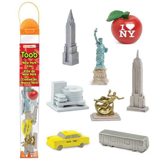 Eight small figurines are shown on a white background: a silver‑gray subway car, a yellow taxi, the green Statue of Liberty, gray Empire State and Chrysler Buildings, the white Guggenheim Museum, a red “I Love NY” apple with a green stem, and a gold Prometheus figure. To the side is the tube-container with all the contents enclosed.