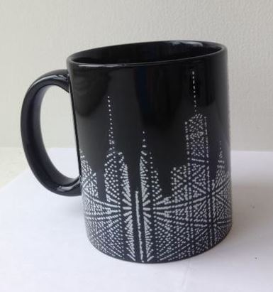 A Museum of the City of New York black ceramic mug with handle. The mug has a white graphic of the stunning Starlight installation which is like a geometric matrix-like cityscape at the bottom of the mug.
