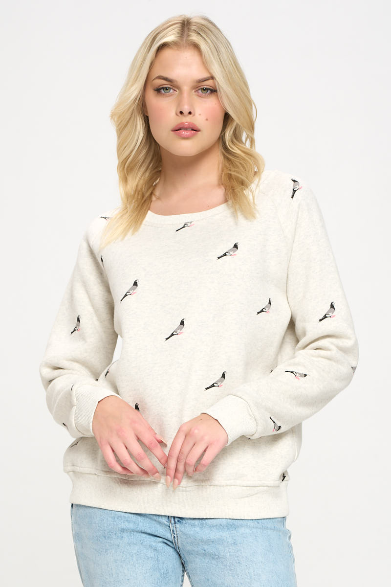 Image shows a woman wearing a crew neck heather gray sweatshirt with a pigeon print evenly repeated across the front, sleeves, and back, forming a continuous all‑over pattern rather than a single central graphic.