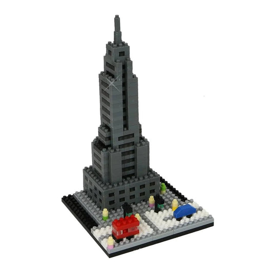 A small, block model of the Empire State Building made from tiny grey bricks. The tower feels tall and narrow, with smooth stepped layers that shrink as they rise. Straight vertical lines guide the fingers up to a thin pointed spire at the top. The model sits on a firm square base with a few simple city details: a small red building, a tiny blue vehicle, and a few miniature figures along the front.