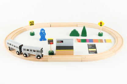 The image shows the contents of the New York City Subway 20‑Piece Wooden Subway Set displayed with the pieces arranged for play: two subway cars, wooden tracks, a platform, a conductor figure, trees, and several signal signs.